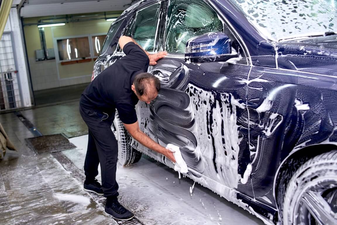 Image depicts a car detailing expert cleaning the exterior of a car.